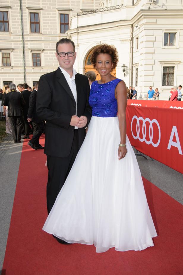 Ein Mann im Anzug und eine Frau in einem Abendkleid posieren auf einem roten Teppich.