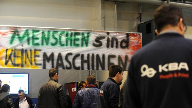 Ein Transparent mit der Aufschrift „Menschen sind keine Maschinen“ hängt in einer Halle.