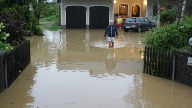 Ein Mann watet durch das überflutete Grundstück eines Wohnhauses.