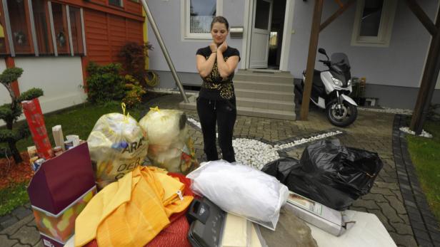 Eine Frau steht vor ihrem Haus neben Säcken mit Müll und aussortierten Gegenständen.