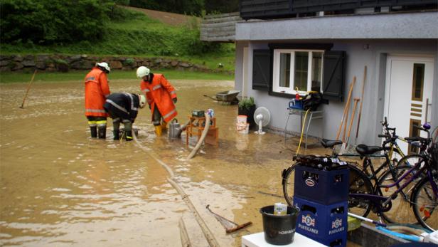 Feuerwehrleute stehen im überfluteten Wasser vor einem Haus.