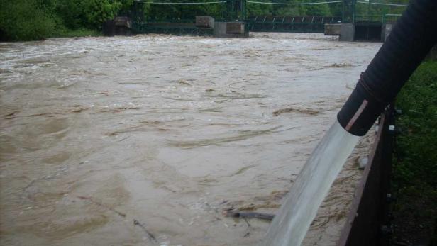 Ein Fluss führt Hochwasser, während Wasser aus einem Rohr abgeleitet wird.