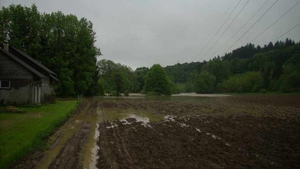 Überschwemmtes Ackerland neben einem Haus unter einem bewölkten Himmel.