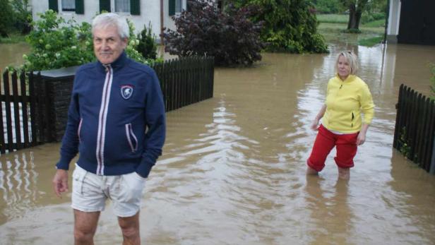 Ein Mann und eine Frau stehen im überfluteten Garten ihres Hauses.
