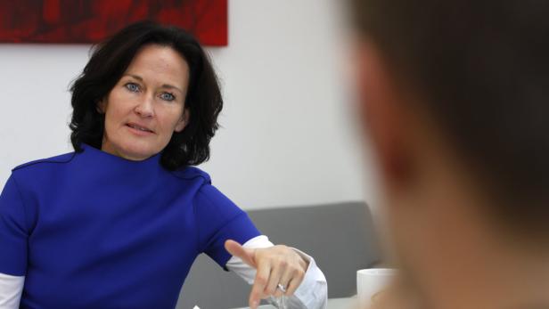 Eine Frau in einem blauen Oberteil gestikuliert in einem Gespräch.