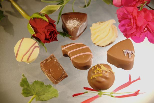 Verschiedene Pralinen liegen dekorativ mit Blüten auf einer Fläche.