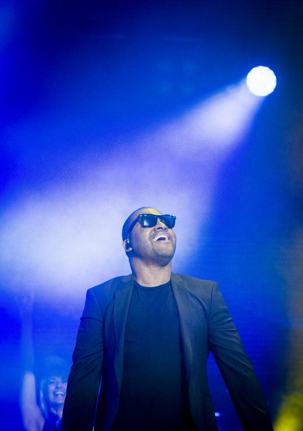 Ein Mann mit Sonnenbrille singt auf einer Bühne unter blauem Licht.