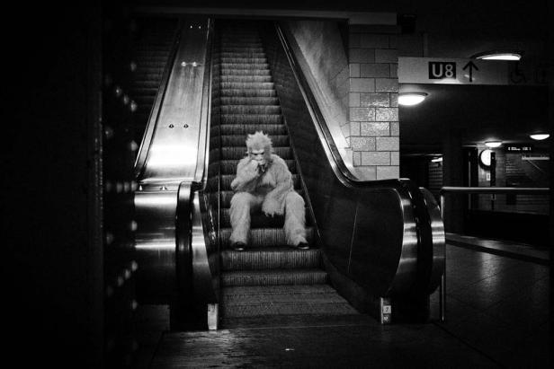 Ein Mann im Yeti-Kostüm sitzt auf einer Rolltreppe in einer U-Bahn-Station.