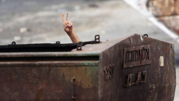 A Palestinian protester gestures as he hides behin