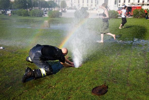 Ein Mann kniet auf einer Wiese und versucht, ein Leck in einem Wasserrohr zu reparieren, während ein Regenbogen entsteht.