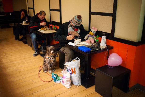 Ein Mann mit Hund isst in einem Restaurant, auf dem Tisch stehen eine Stoffente und ein Herzluftballon.