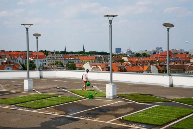Eine Person bewässert Rasenflächen auf einem Parkdeck mit Blick auf eine Stadt.