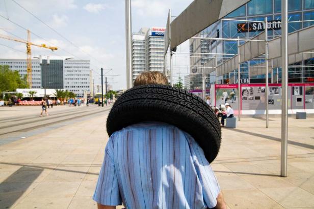 Ein Mann trägt einen Reifen über seinen Schultern auf einem öffentlichen Platz in Berlin.