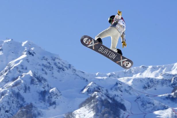 Ein Snowboarder springt vor einer verschneiten Bergkulisse mit einem Burton-Board.