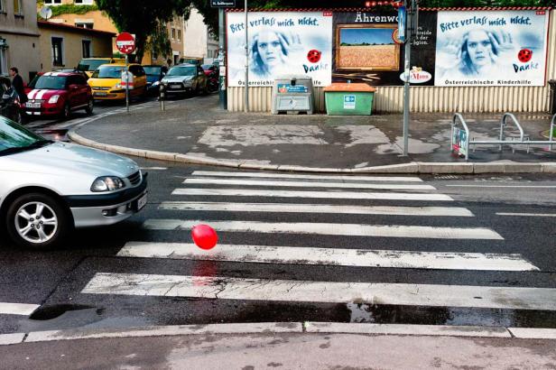 Ein roter Ballon liegt auf einem Zebrastreifen in einer städtischen Umgebung.