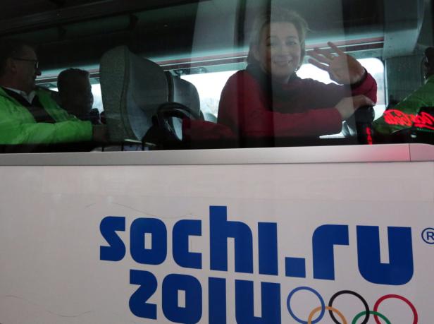 Eine Frau winkt aus einem Bus mit der Aufschrift „sochi.ru 2014“.