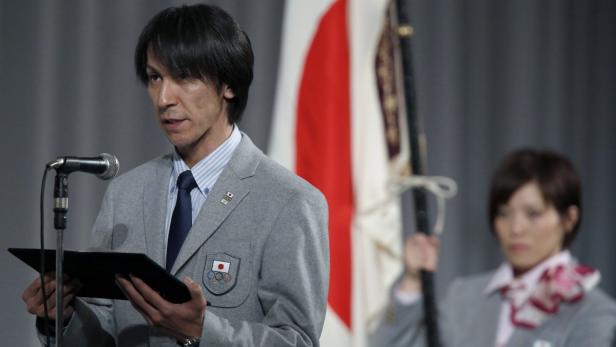 Ein Mann im Anzug spricht am Mikrofon vor der japanischen Flagge.