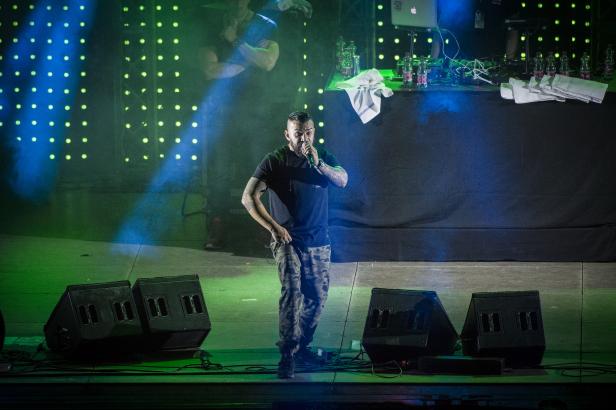 Ein Rapper mit Tätowierungen performt auf einer Bühne mit grüner Beleuchtung.