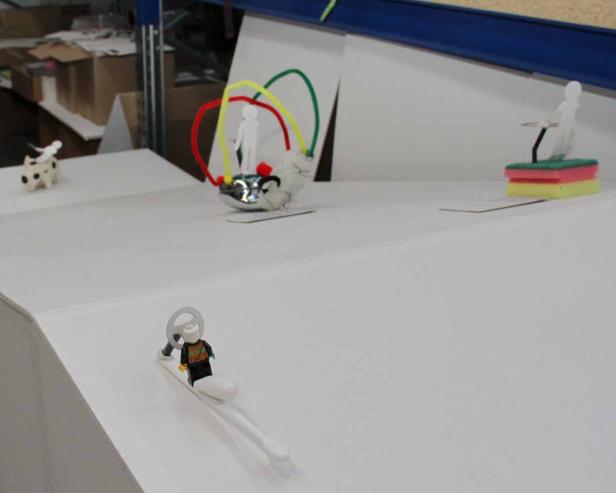 Eine surreale Szene mit verschiedenen kleinen Figuren und Objekten auf einer weißen Oberfläche.