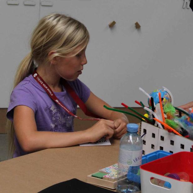 Ein blondes Mädchen bastelt an einem Tisch mit Pfeifenreinigern und einem Globus.
