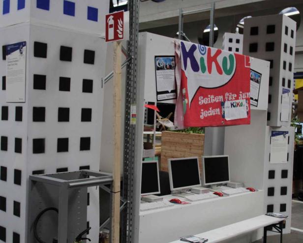 Ein Messestand mit Computern und einer Dekoration, die eine Stadtlandschaft darstellt.