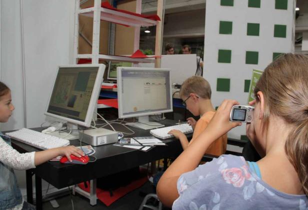 Kinder sitzen an Computern, während ein Mädchen ein Foto macht.