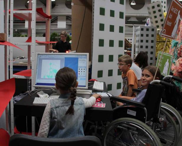 Ein Mädchen arbeitet an einem Computer, während ein anderes Mädchen im Rollstuhl daneben sitzt.