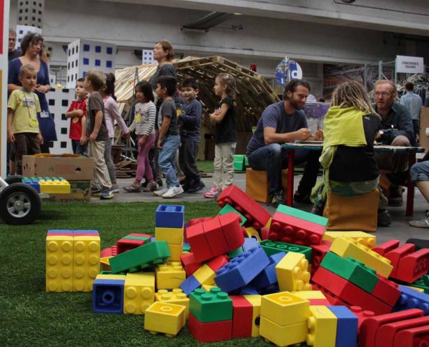 Eine Gruppe von Kindern spielt mit übergroßen Legosteinen in einem Innenraum.