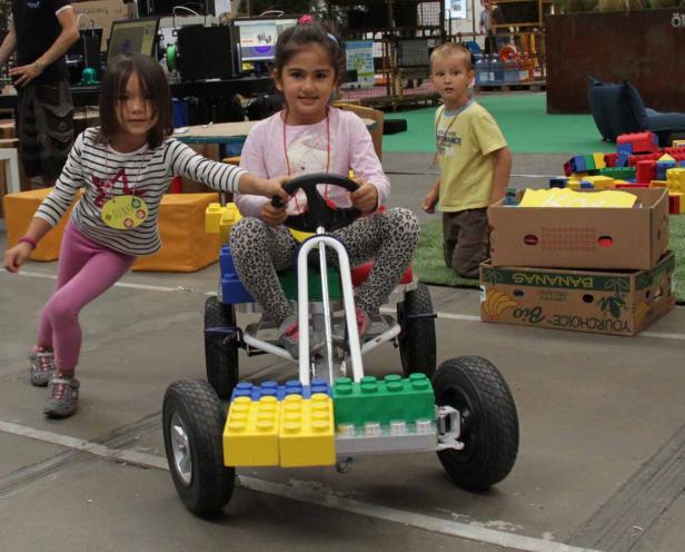 Zwei Mädchen und ein Junge spielen mit einem Go-Kart, das mit Legosteinen verziert ist.