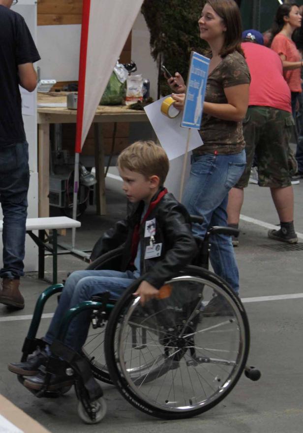 Ein Junge im Rollstuhl wird von einer Frau begleitet.