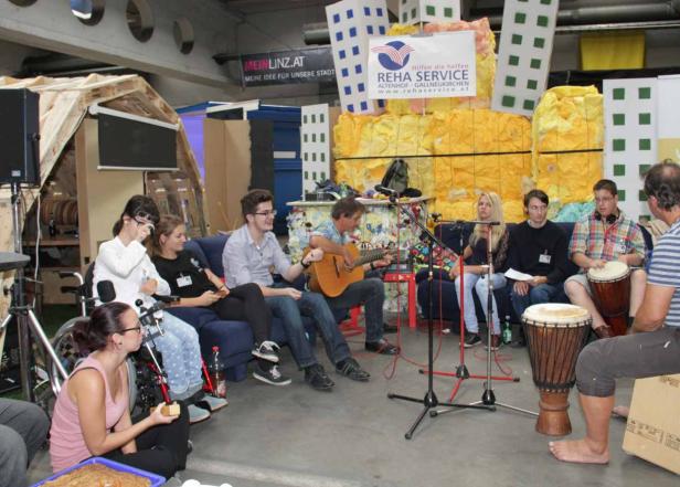 Eine Gruppe von Menschen sitzt zusammen, einige spielen Gitarre und Trommeln.