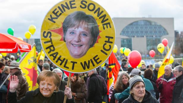 Demonstranten halten Schilder mit dem Konterfei von Angela Merkel und der Aufschrift „Keine Sonne strahlt wie ich“.