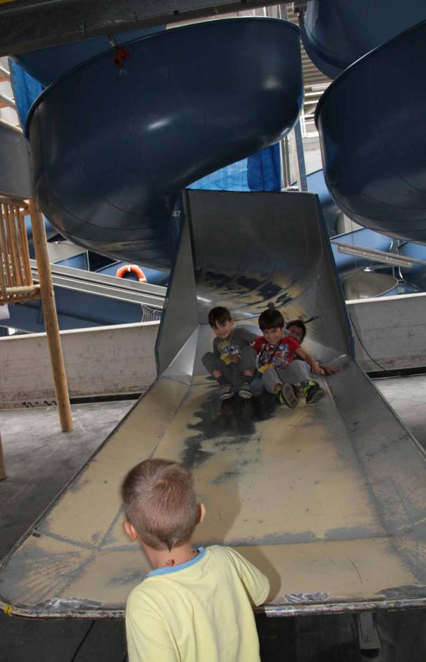 Drei Kinder rutschen eine lange Metallrutsche hinunter.