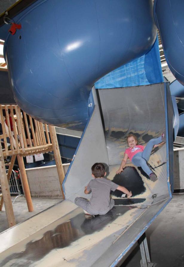Zwei Kinder rutschen eine große Metallrutsche hinunter.