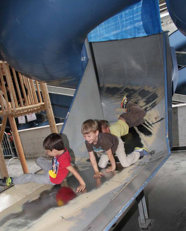 Drei Kinder rutschen eine große Metallrutsche hinunter.