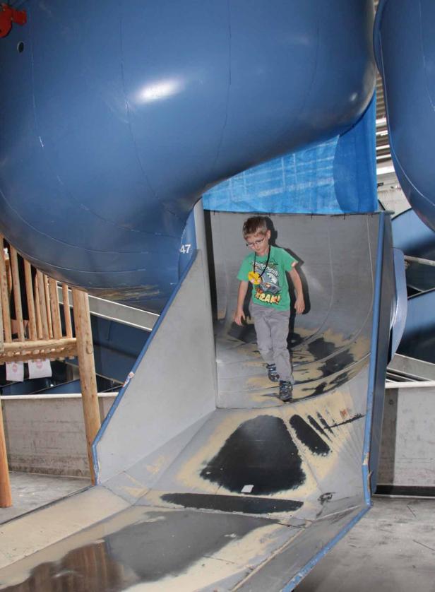 Ein Junge mit Brille rutscht eine graue Rutsche herunter.