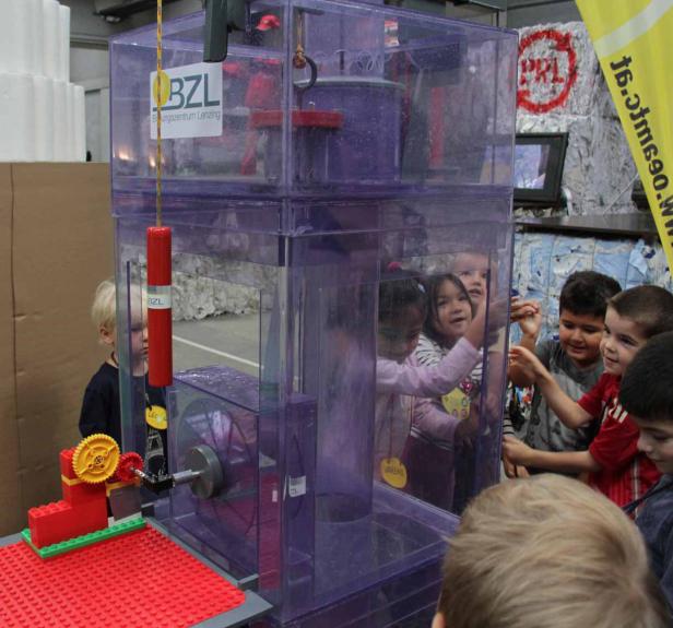 Kinder beobachten eine Vorrichtung in einem transparenten, violetten Gehäuse.