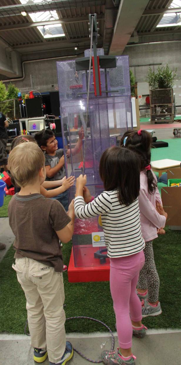Eine Gruppe Kinder spielt mit einer Wasserinstallation in einem Innenraum.