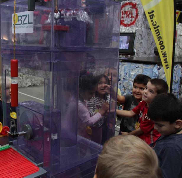 Eine Gruppe Kinder betrachtet neugierig eine Maschine aus transparentem Kunststoff.