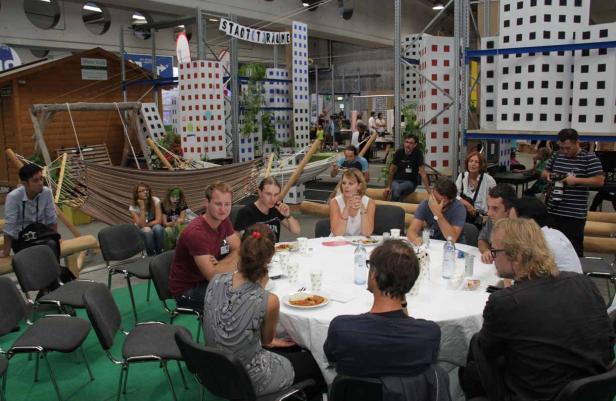 Eine Gruppe von Menschen sitzt an einem runden Tisch in einem Raum mit dem Thema „Stadträume“.