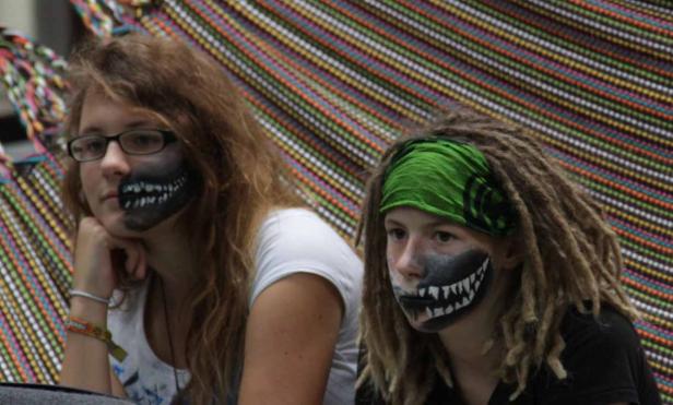 Zwei junge Frauen mit gruseliger Gesichtsbemalung sitzen vor einem bunten Hintergrund.