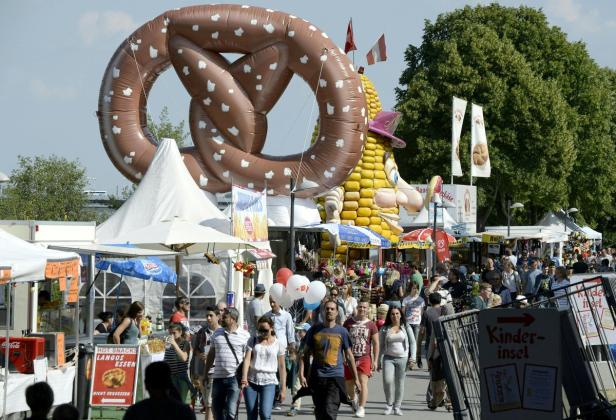Ein belebtes Stadtfest mit einem riesigen Brezel-Ballon und einem Maiskolben-Maskottchen.