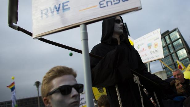 Eine als Tod verkleidete Person demonstriert mit Schildern von RWE und Umweltorganisationen.
