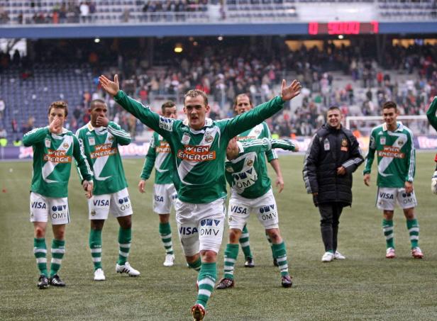Ein Fußballspieler von Rapid Wien jubelt mit ausgestreckten Armen auf dem Spielfeld.