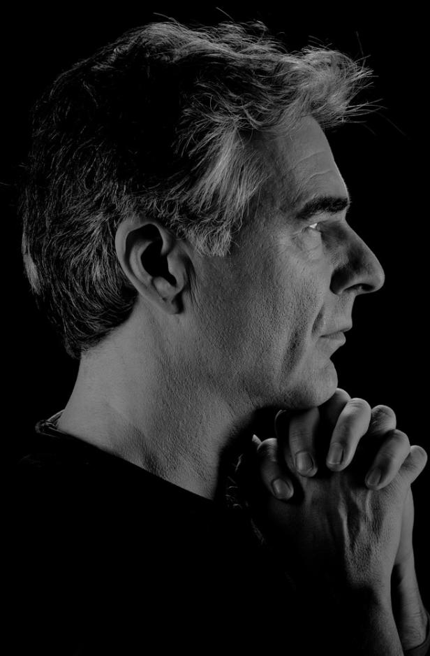 Ein Mann mit grau meliertem Haar im Profil, die Hände gefaltet vor dem Gesicht.
