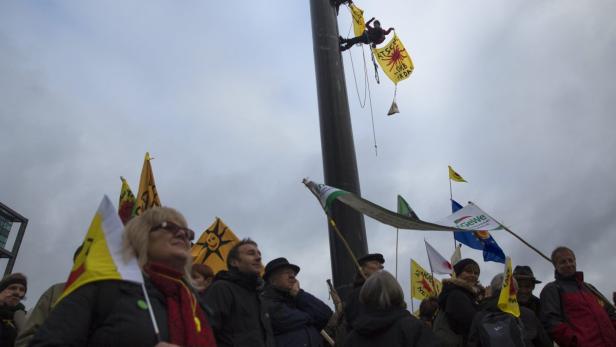 Ein Demonstrant klettert an einem Mast hoch, umgeben von protestierenden Menschen mit Fahnen.