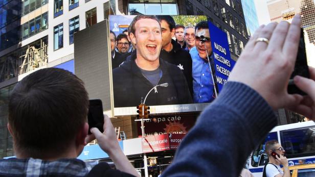 Passanten fotografieren eine große Werbetafel am Times Square mit Mark Zuckerberg.