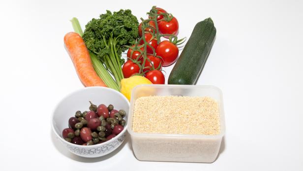 Eine Auswahl an frischem Gemüse, Oliven und Getreide auf einem weißen Hintergrund.