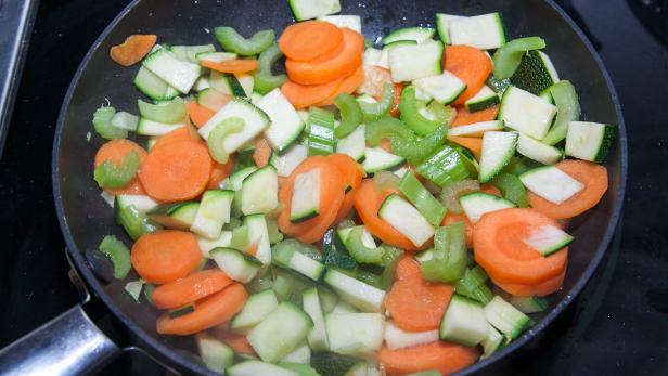 Geschnittene Karotten, Zucchini und Sellerie werden in einer Pfanne gebraten.