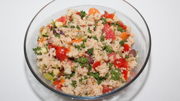 Ein Glasbehälter gefüllt mit Couscous-Salat mit Gemüse wie Tomaten, Zucchini und Karotten.